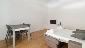 Una habitación con cama, televisión, escritorio y sillas, y un mueble pequeño.