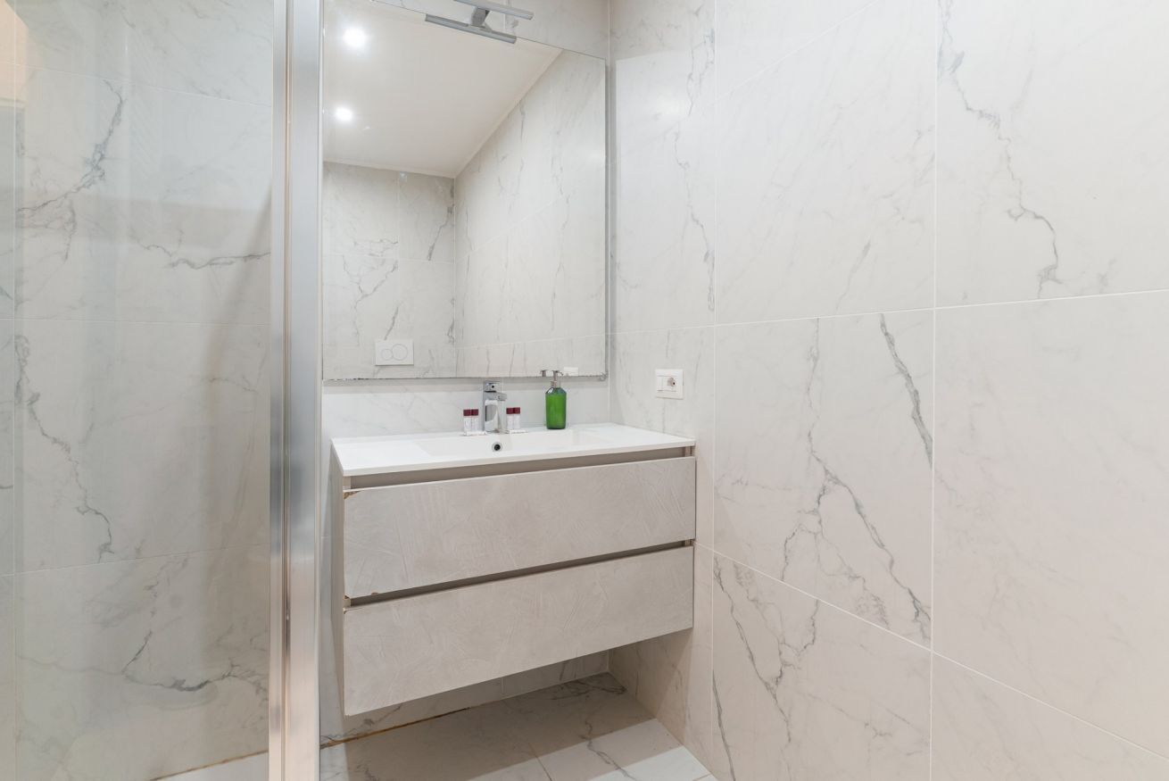 A bathroom with a white marble sink, a mirror, and a glass shower enclosure.