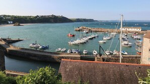 A harbor with boats docked, a stone wall, and a building with a red roof. - Longmoor (Tenby)