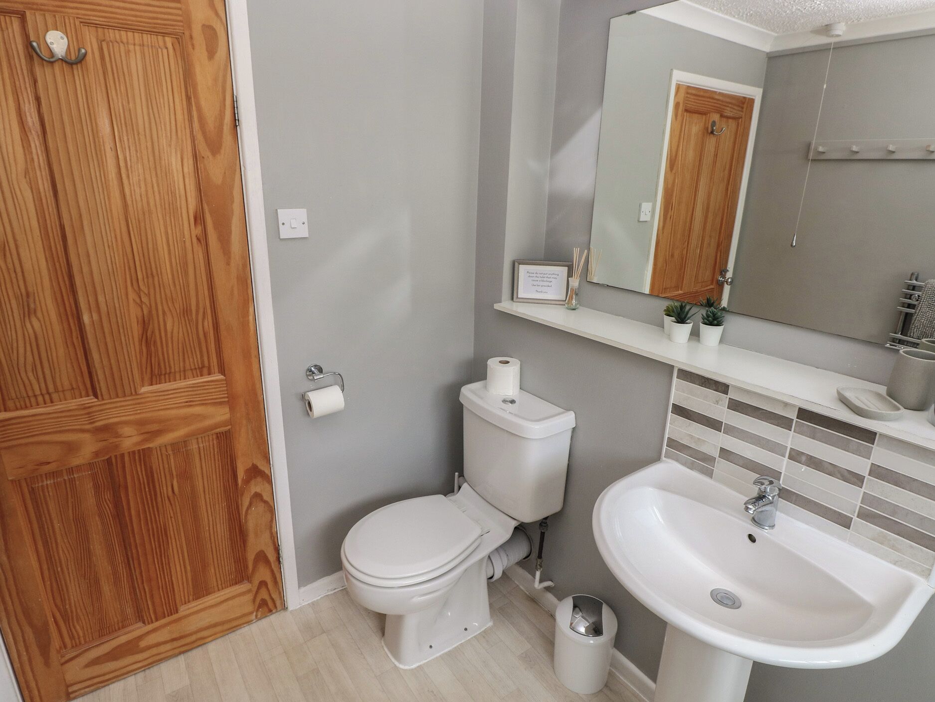 A bathroom with a wooden door, a toilet, a sink, and a mirror.