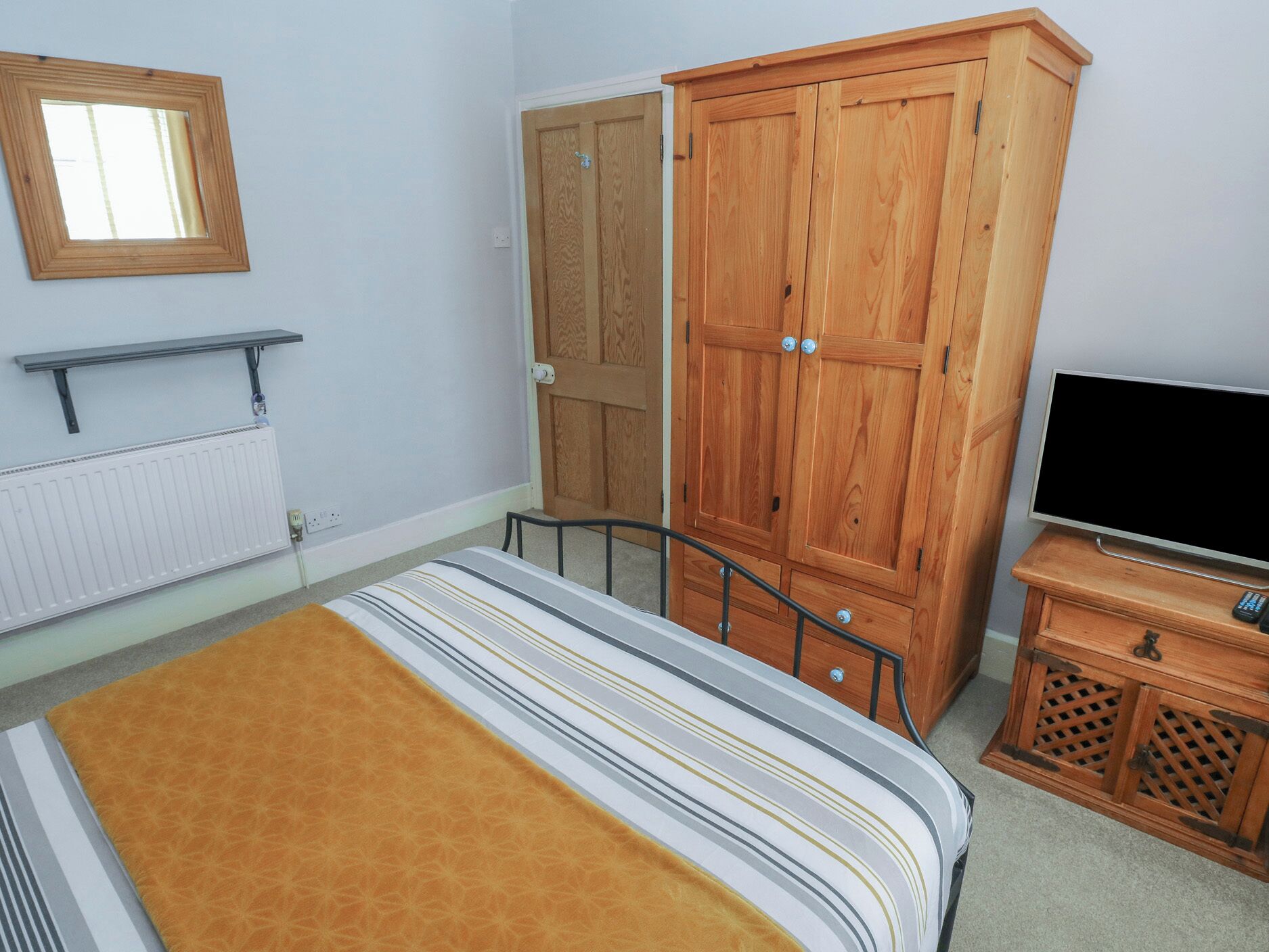 A bedroom with a bed, wooden wardrobe, TV stand, and a window.
