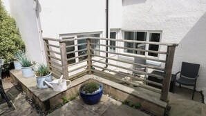 A small outdoor patio area with a wooden fence, potted plants, a white watering can, and a blue pot. - Longmoor (Tenby)