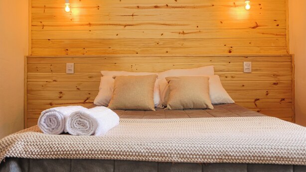 A neatly made bed with rolled towels, a wooden headboard, and two wall-mounted lights. - | White cabin | Fireplace, fireplace, tranquility, ideal for families and friends (Gonçalves)