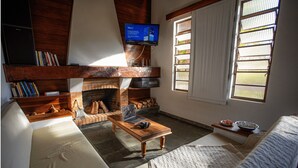 A living room with a fireplace, a television mounted above it, and a sofa. - | White cabin | Fireplace, fireplace, tranquility, ideal for families and friends (Gonçalves)