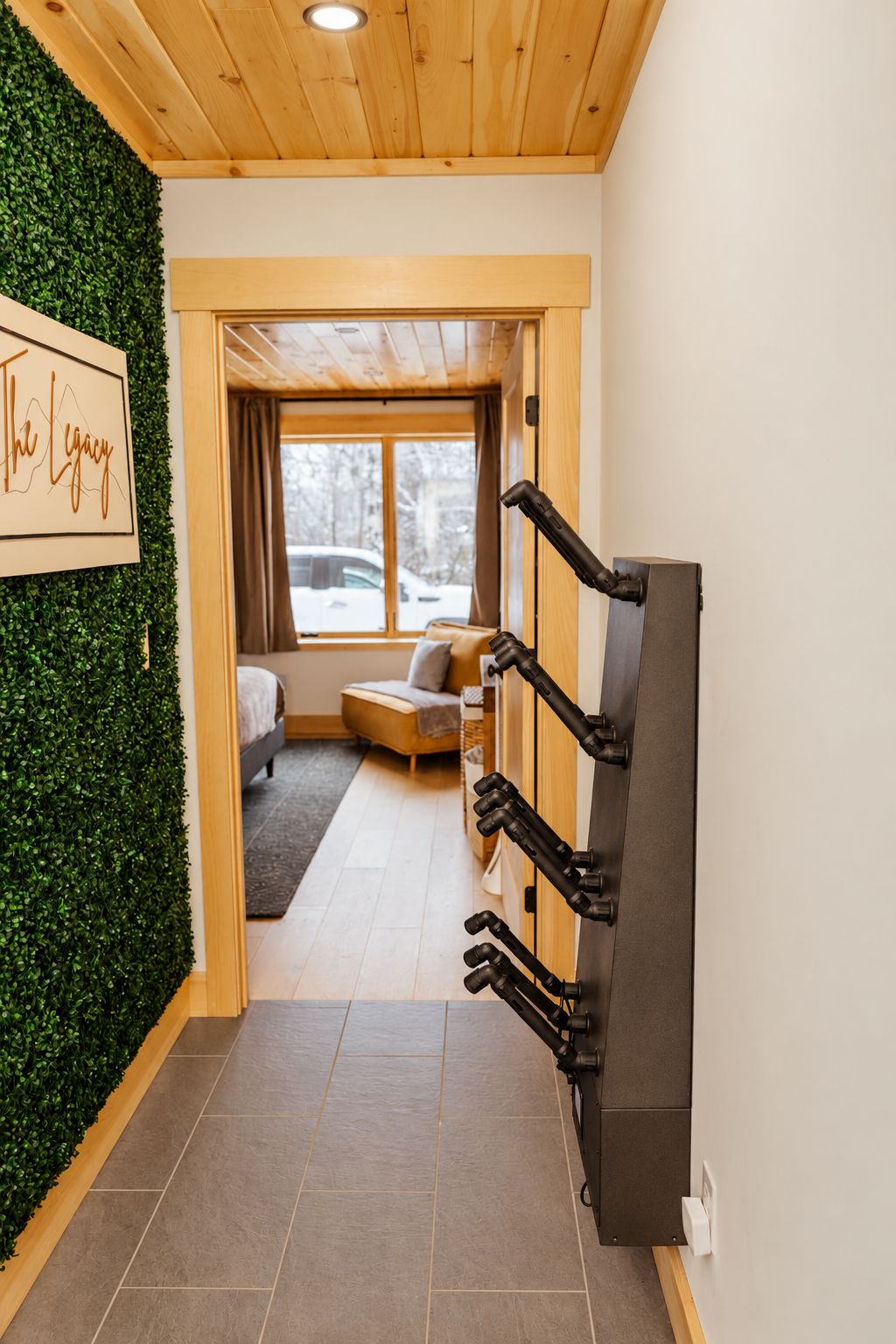 Un interior moderno con techo de madera, pared verde, cámara montada, cama y ventana con vista a árboles.