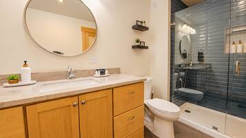 Une salle de bain avec un meuble-lavabo à deux vasques, des toilettes et une douche séparée par une paroi en verre.