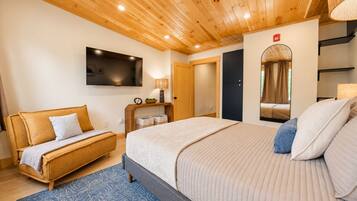 Ein Hotelzimmer mit Bett, Sofa, Fernseher, Spiegel und Holzboden.