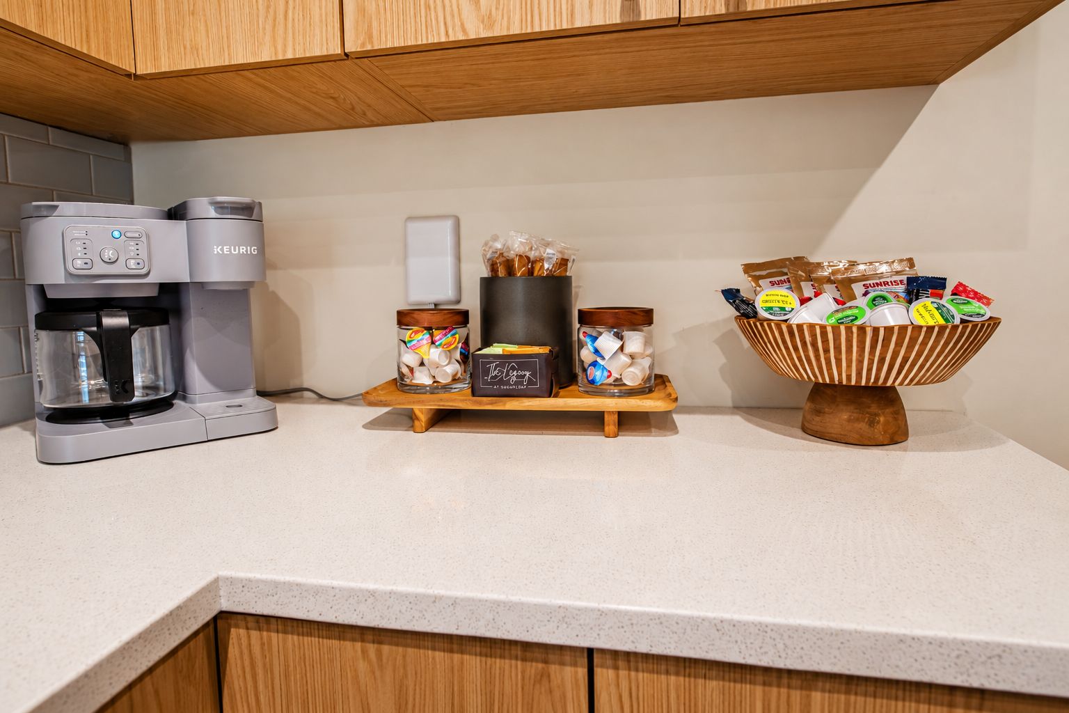 A kitchen with a coffee maker, a jar of marshmallows, a container of sugar, and a bowl of snacks on the counter.