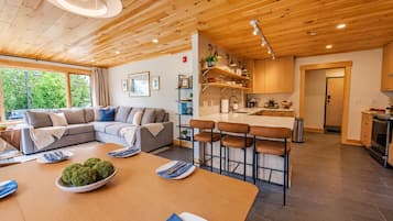 A modern interior with a wooden ceiling, a living area with a sofa and a dining table set, and a kitchen with bar stools.