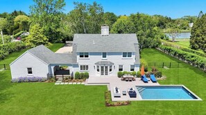 A two-story house with a swimming pool, a patio with outdoor furniture, and a well-maintained lawn.