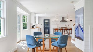 Une cuisine moderne avec des meubles blancs, une porte noire et un coin repas comprenant une table en verre et des chaises bleues.