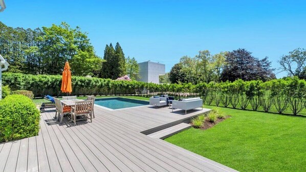 A wooden deck with a pool, outdoor furniture, and a well-maintained lawn.