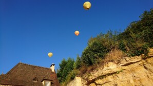 A building with a brick roof and a chimney, surrounded by greenery and a cliff. - CHAMBRE D'HÖTE AT THE FOOT OF THE CHATEAU SLIDING-SCALE RATES PLUS 2 NIGHTS WEEKEND INCLUDED (Castelnaud-la-Chapelle)