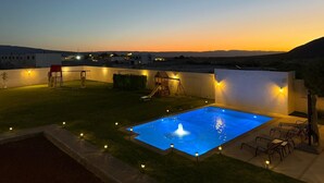 A rooftop pool with a fountain, surrounded by outdoor seating and a slide, set against a sunset backdrop. - Departamentos Aremay (Cuatro Ciénegas)