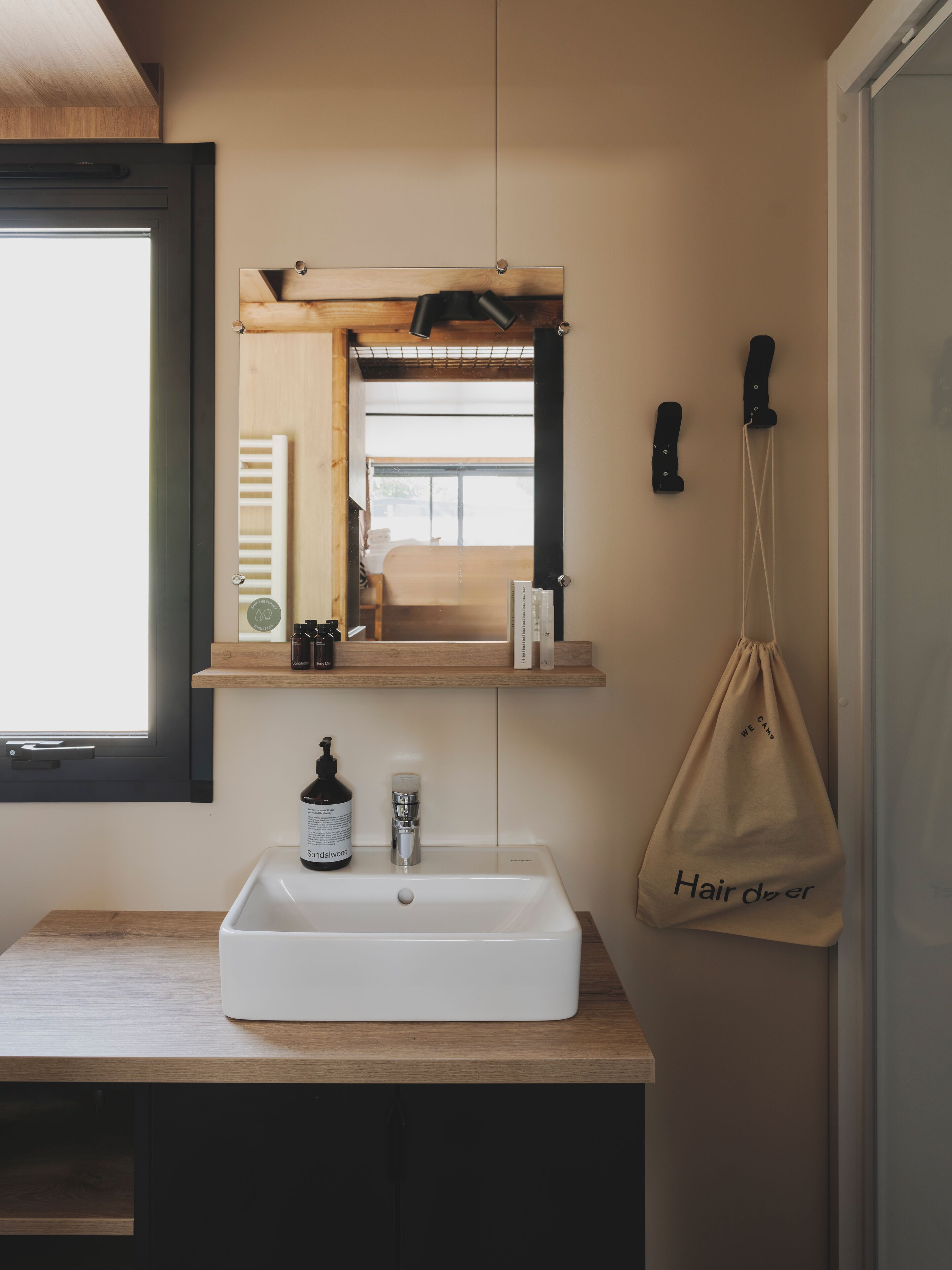 Un bagno con un lavandino bianco, uno specchio e una borsa appesa con l'indicazione 'Asciugacapelli'.