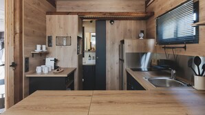 A compact kitchen with wooden cabinetry, a built-in stove, a sink, and a window with blinds. - wecamp Jávea (Javea)