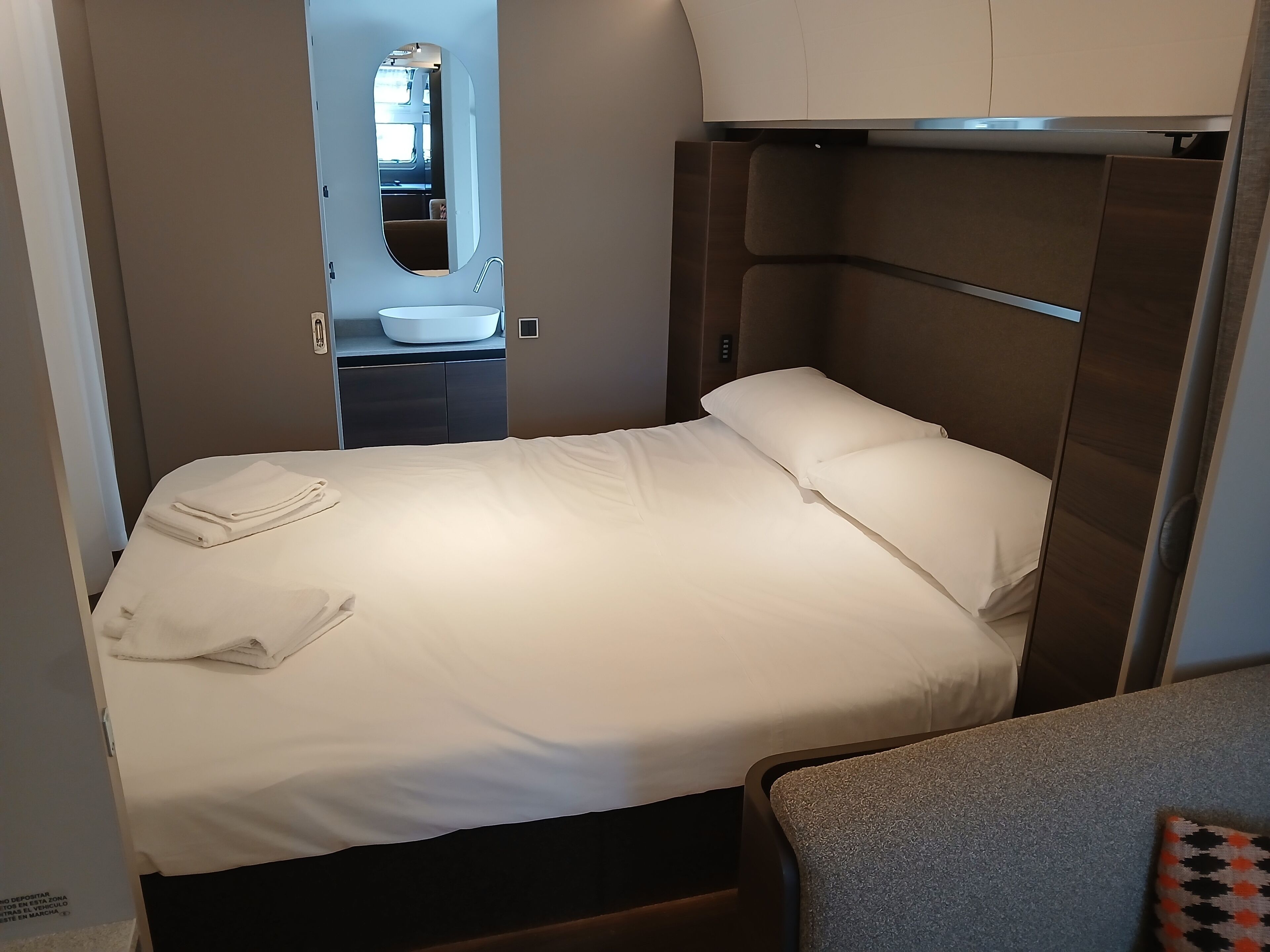 A compact bedroom with a single bed, a built-in vanity with a mirror, and a small seating area.