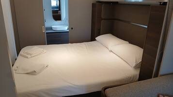 A compact bedroom with a single bed, a built-in vanity with a mirror, and a small seating area.