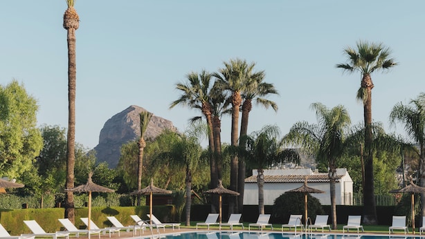 A pool area with lounge chairs, palm trees, and a mountain in the background. - wecamp Jávea (Javea)