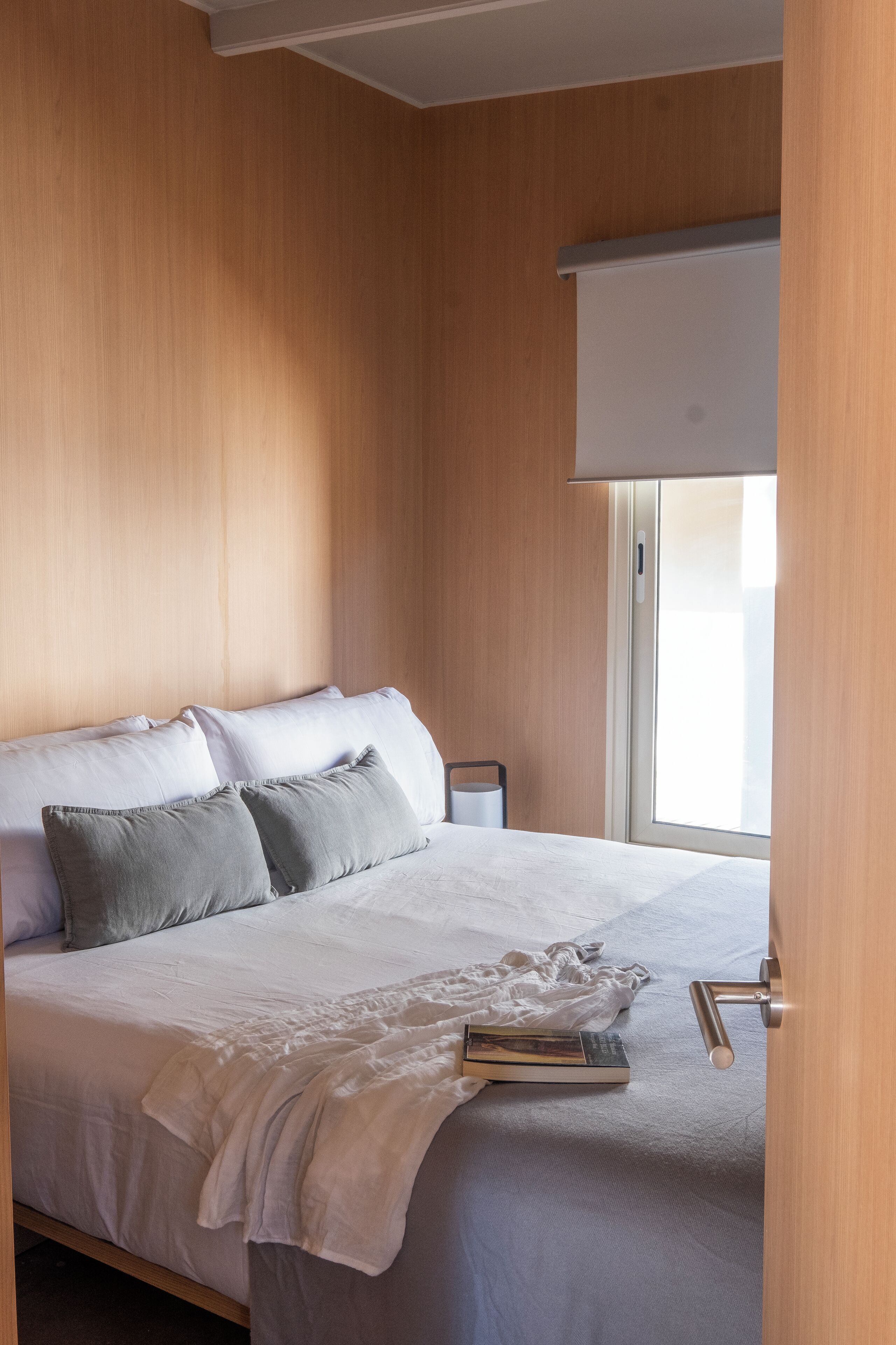 Una cama bien hecha con almohadas, una mesita de noche y una ventana con persianas.