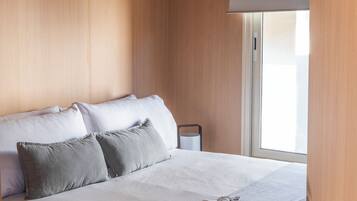 Una cama bien hecha con almohadas, una mesita de noche y una ventana con persianas.