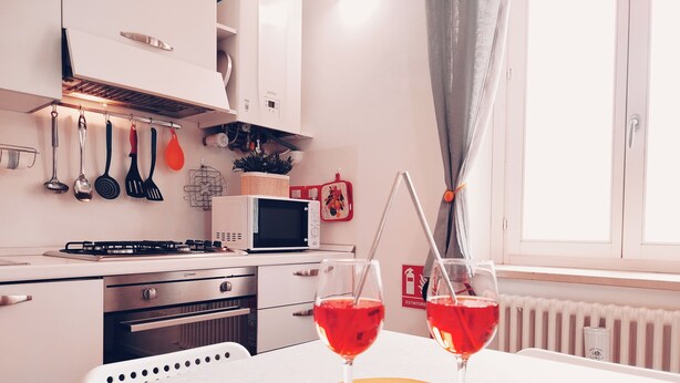 A modern kitchen with a gas stove, microwave, and oven. There are two wine glasses on a table with a red drink.