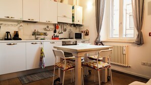 A modern kitchen with white cabinets, a dining table with chairs, a microwave, and a window with curtains.