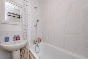 A bathroom with a white sink, a mirror, a shower, and tiled walls.