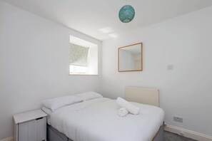 A bedroom with a bed, a nightstand, a window, a mirror, and a ceiling light fixture.