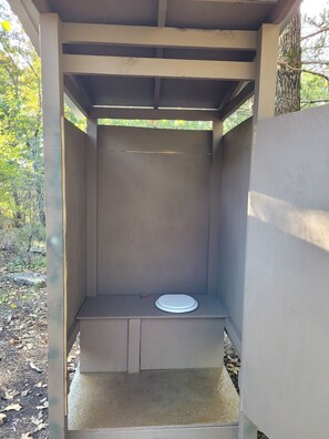 A small, enclosed outdoor shower with a white seat and a concrete floor.