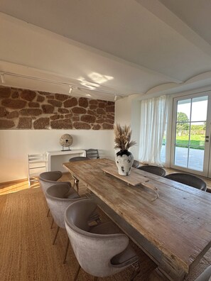 A dining area with a rustic wooden table, grey upholstered chairs, a stone wall, and a view through large windows. - 360 m² country house with pool, fireplace & large garden near Leipzig (Frohburg OT Ottenhain)