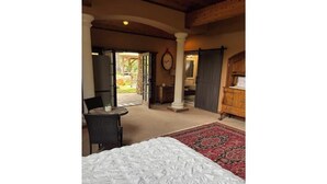 Ein Schlafzimmer mit Bett, kleinem Tisch, Stuhl und Blick auf den Garten durch eine geöffnete Tür.
