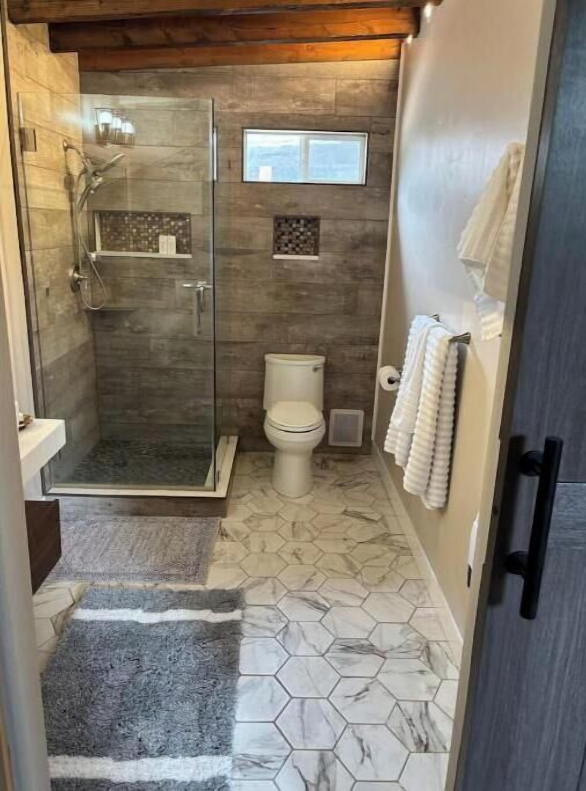 A compact bathroom with a glass shower enclosure, a toilet, and a small window.