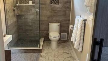 A compact bathroom with a glass shower enclosure, a toilet, and a small window.