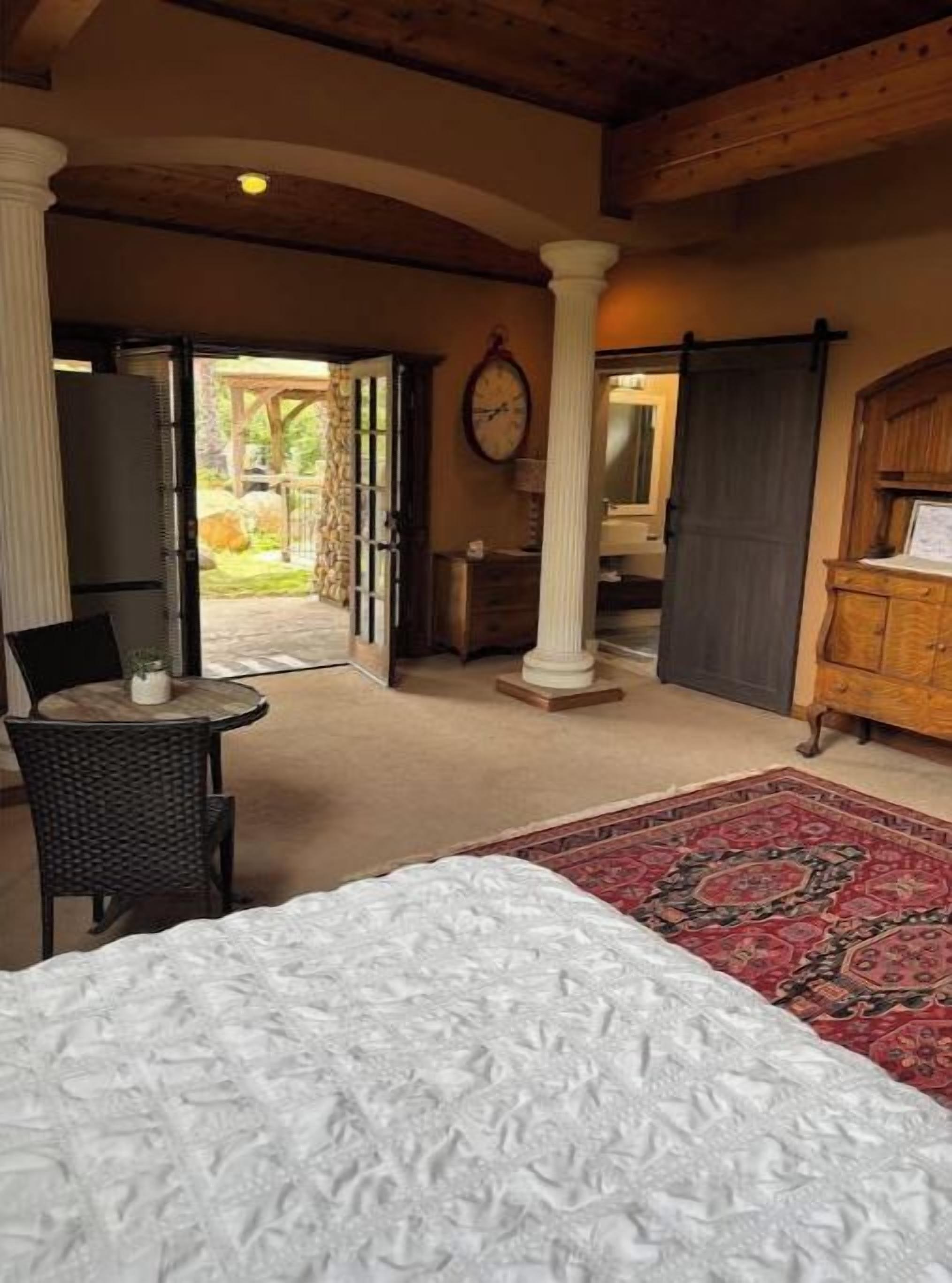 Un dormitorio con una cama, una mesita, una silla y vistas al jardín a través de una puerta abierta.