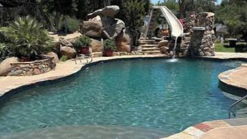 Une piscine avec un toboggan, entourée de rochers et d’arbres.