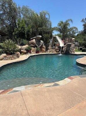 A swimming pool with a slide, surrounded by rocks and trees. - Grand Studio with exclusive resort amenities. (Alpine)