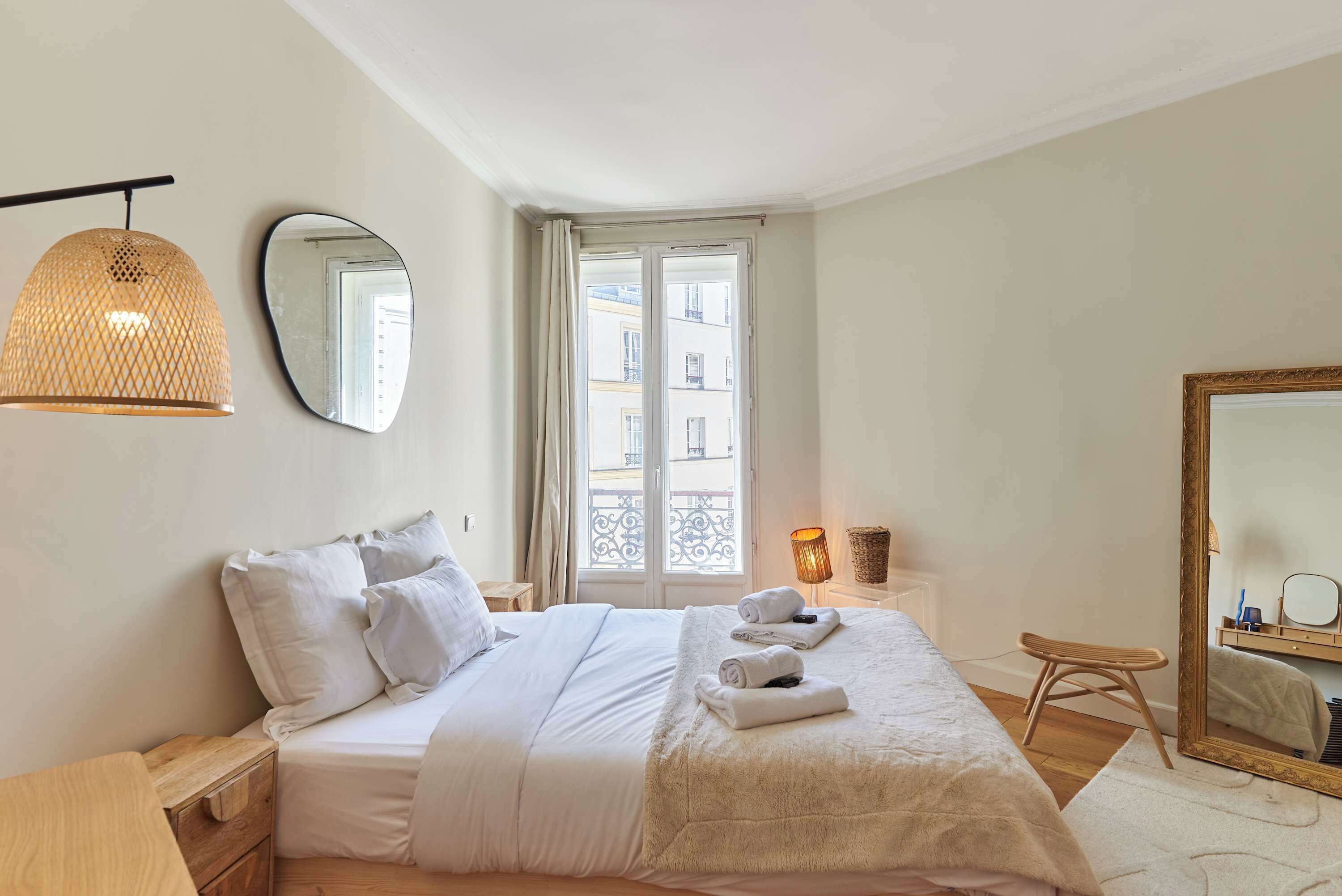 A bedroom with a bed, bedside tables, a mirror, a window, and a hanging light fixture.