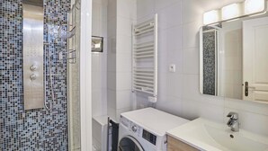 A modern bathroom with a washing machine, a sink, a mirror, and a shower area. - Charming Apartment  with AC- Heart of Le Marais (Paris)