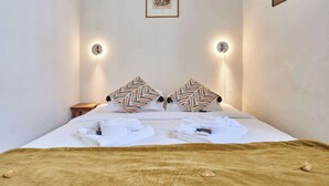 A neatly made bed with two decorative pillows, a bedside table, and wall-mounted lights. - Charming Apartment  with AC- Heart of Le Marais (Paris)