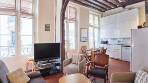 A living room with a flat-screen TV, sofas, a coffee table, and a dining area with chairs and a table. - Charming Apartment  with AC- Heart of Le Marais (Paris)