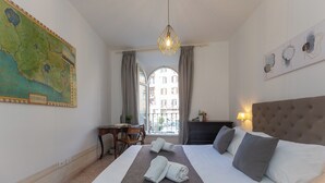 A hotel room with a bed, a desk, a map on the wall, and a view of buildings outside. - Rental in Rome Angelico Apartment (Rome)