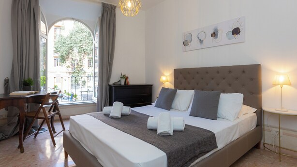 A neatly arranged bedroom with a bed, bedside table, lamp, and a window with curtains. - Rental in Rome Angelico Apartment (Rome)