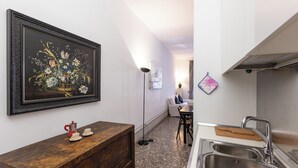 A kitchen with a sink, a wooden table with a red coffee maker, a framed floral painting, and a floor lamp. - Rental in Rome Angelico Apartment (Rome)