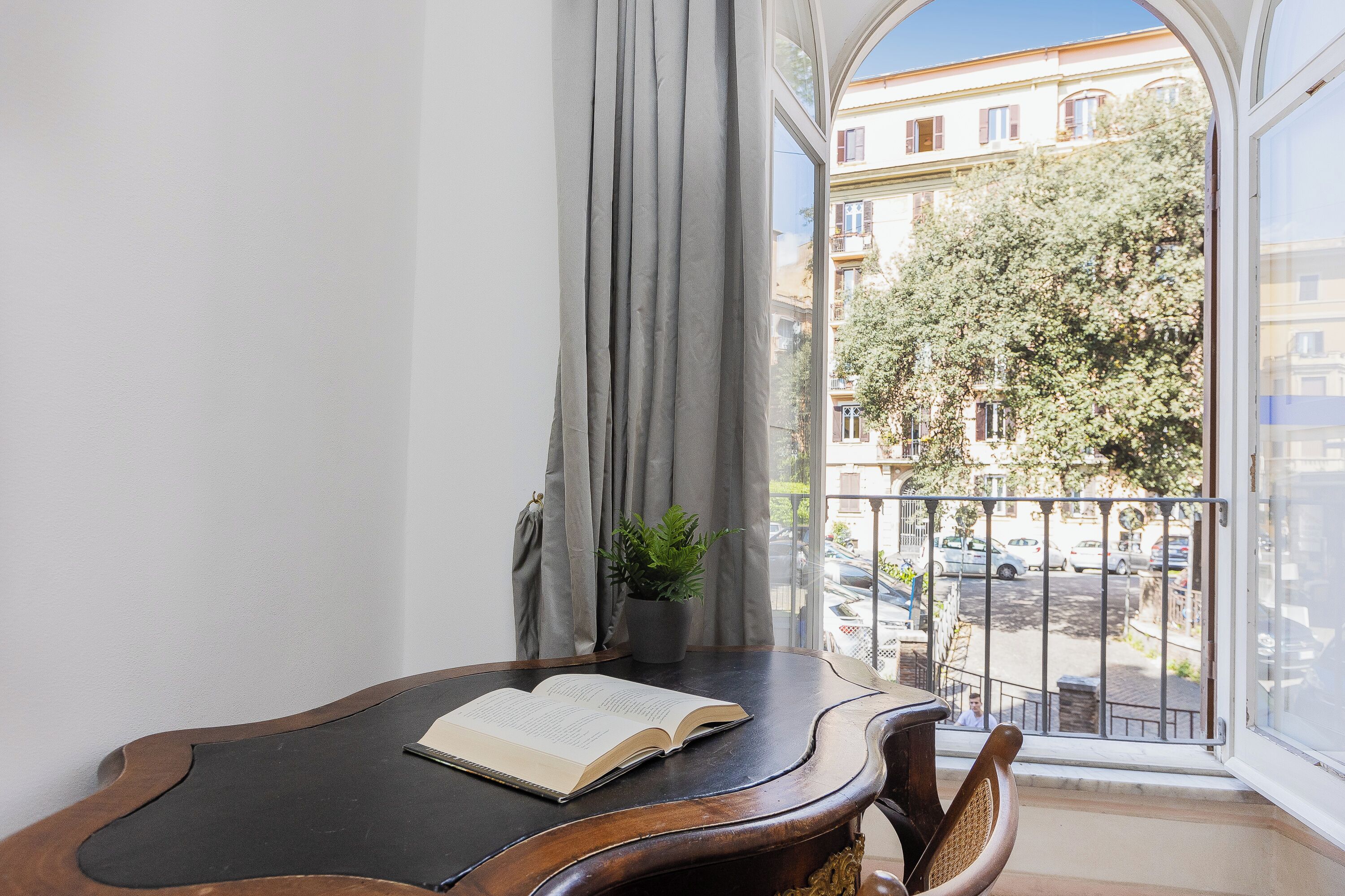 Una habitación con una mesa de madera, una planta en maceta y vistas a un balcón con barandilla y coches estacionados.