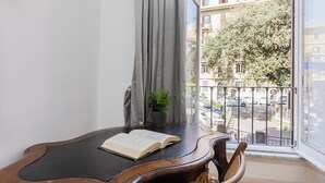 A room with a wooden table, a potted plant, and a view of a balcony with a railing and parked cars. - Rental in Rome Angelico Apartment (Rome)
