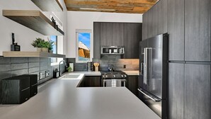 A modern kitchen with dark cabinetry, a stainless steel refrigerator, and a built-in oven. - Mountain Views Eden Cabin w/ Hot Tub & Fireplace (Eden)