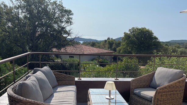 A sunlit outdoor seating area with wicker furniture and a glass-top table, overlooking a scenic landscape. - Apartment in residence with swimming pool and janitor, walking distance to the beach (Zonza)