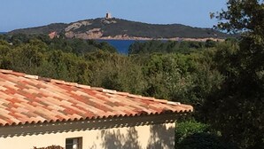 A building with a tiled roof, surrounded by greenery and a hill with a tower in the background. - Apartment in residence with swimming pool and janitor, walking distance to the beach (Zonza)