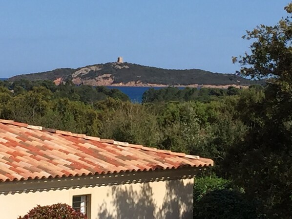 A building with a tiled roof, surrounded by greenery and a hill with a tower in the background.